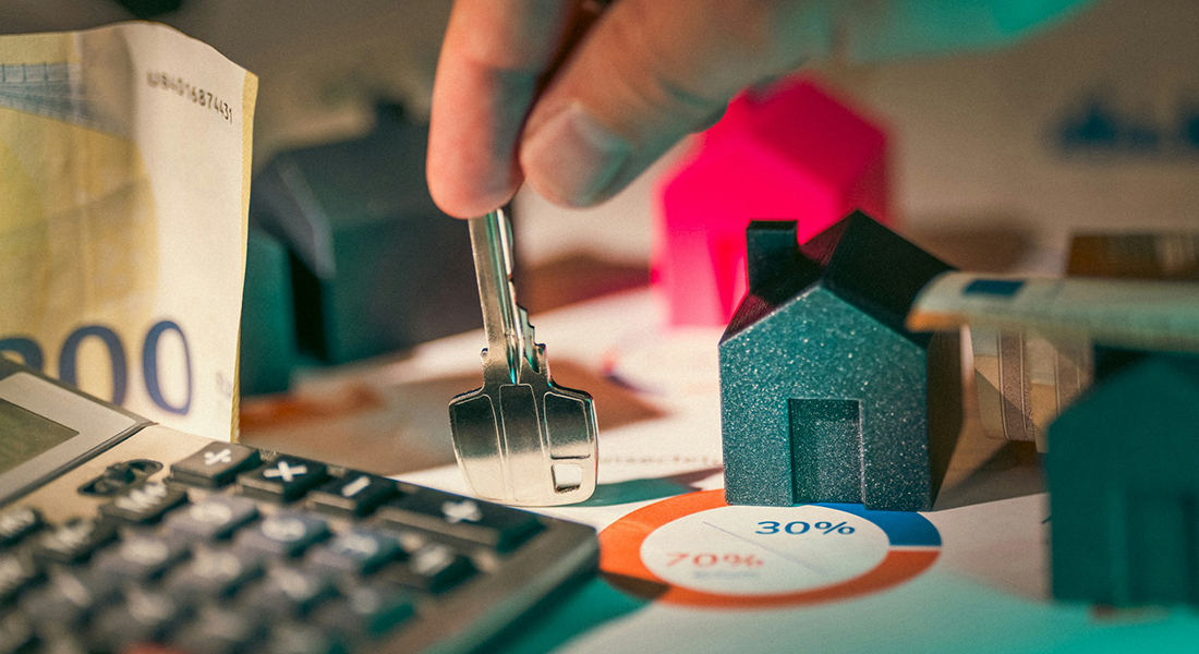 Skrivebord med lommeregner, pengeseddel og model af hus.