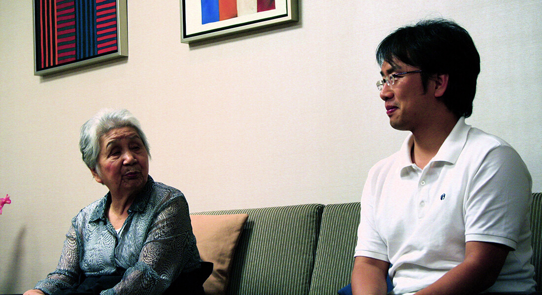 Ældre koreansk kvinde sidder med sin søn i en sofa.