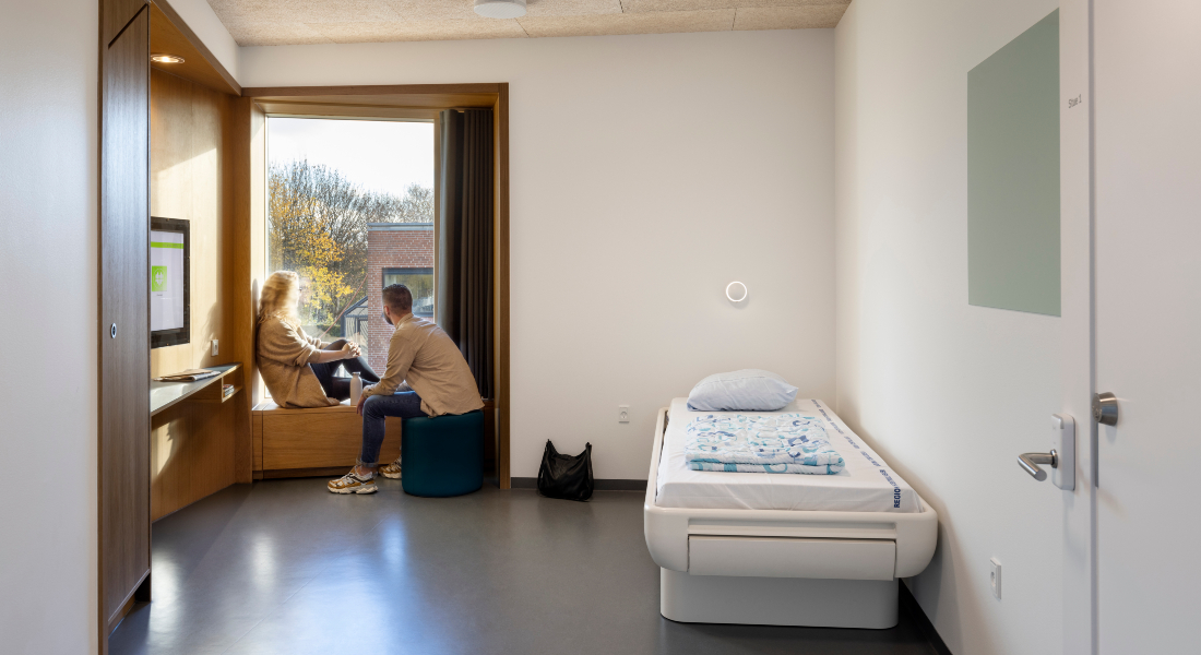 To personer sidder i vinduet i et sengeværelse med en enkeltseng og hvide vægge.