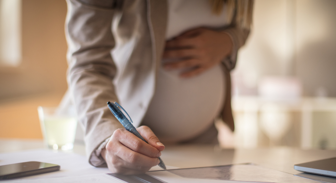Gravid kvinde der bøjer sig forover for at skrive på et stykke papir